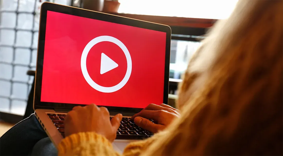 Woman using a laptop with a video on screen