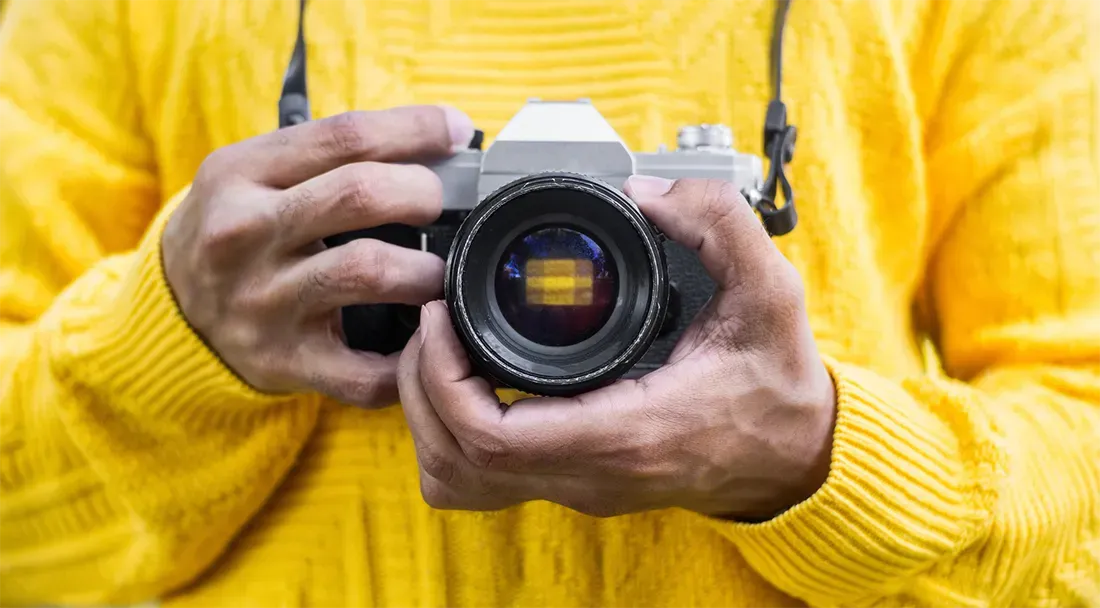 a close up of a man in a yellow sweater holding a high end camera